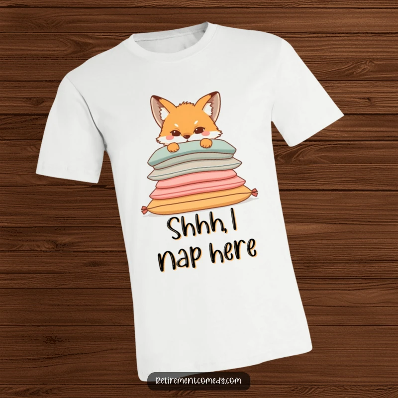 Funny t-shirt featuring a sly fox with a mischievous grin peeking from behind a stack of soft, inviting cushions, embodying cozy sneakiness.